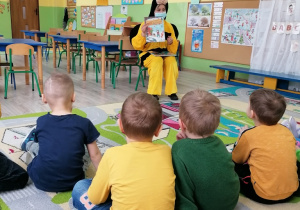 Dzieci słuchają książki czytanej przez panią bibliotekarkę w przebraniu pszczółki.