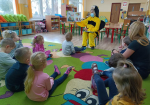 Dzieci słuchają bajki czytaną przez panią bibliotekarkę w przebraniu pszczółki.