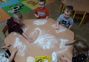 Dzieci rysują palcem wzory na mące.