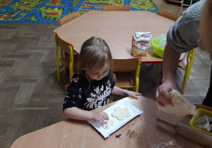 Dzieci z nauczycielką za pomocą foremek wykrawają elementy z masy solnej.