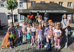 Grupa uśmiechniętych dzieci stojąca przy namiocie Bazy Logistycznej