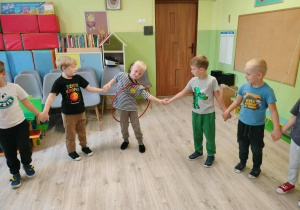 Dzieci trzymające się za ręce, biorące udział w zabawie przekładając sobie hula-hop.