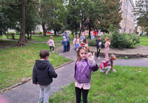 Dziewczynka trzymająca kasztan, wokół grupy dzieci szukających śmieci.