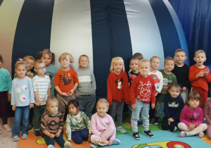Grupa dzieci z nauczycielką siedząca i stojąca na tle kopuły planetarium.