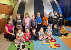 Grupa dzieci z nauczycielką siedząca i stojąca na tle kopuły planetarium.