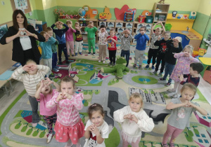 Grupa dzieci stojąca w kole wraz z nauczycielką. Tworzą znak serca ze swoich dłoni pokazują do zdjęcia.