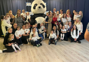 Grupa dzieci i rodziców stojąca obok ogromnego misia.