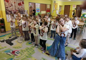 dzieci ubrane w brązowe bluzki z misami i uszami misiów na głowach tańczą i pokazują ze śpią.