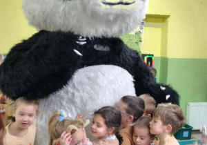 Dzieci przytulają wielkiego misia pandę.