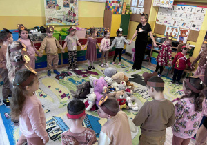 Dzieci stoją w kole na środku leżą pluszowe misie.