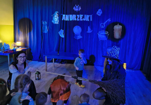 Kobiety przebrane za wiedzmy trzymają miotłę a dziecko pod nią przechodzą.