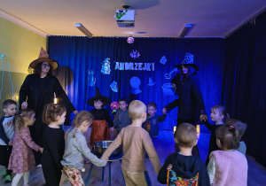 Dzieci i dwie wiedzmy stoją w kole dokoła miski z wodą.