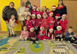 Grupa dzieci w czerwonych strojach i czapkach Mikołajów. Dzieci trzymają w dłoniach wykonane mydełka.
