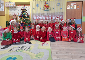 Grupa dzieci w czerwonych strojach i czapkach Mikołajów.