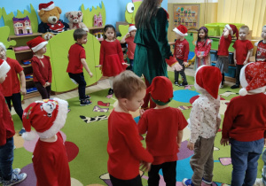Grupa dzieci w czerwonych strojach i czapkach Mikołajów stoją w kole i tańczą. .