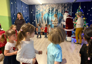 Dzieci w odświętnych strojach tańczą w kole z Świętym Mikołajem.