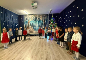 Dzieci w odświętnych strojach stoją w kole i śpiewaj a piosenkę..