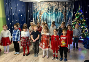 Dzieci w odświętnych strojach stoją i śpiewaj a piosenkę.