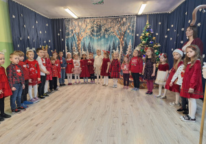 Dzieci w odświętnych strojach stoją w kole i śpiewaj a piosenkę.