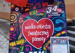 Sztaluga z plakatem Wielkiej Orkiestry Świątecznej Pomocy - 34 finał - postawiona przed budynkiem przedszkola.