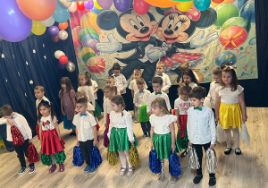 Dzieci ubrane odświętnie trzymające w dłoniach kolorowe pompony.