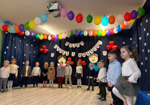 Grupa dzieci stojąca podczas występu z okazji Dnia Babci i Dziadka. Ubrani w eleganckie stroje