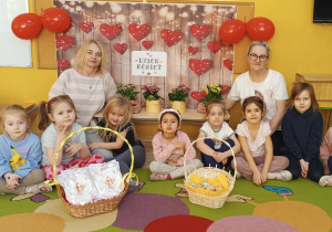 Grupa dziewczynek "Żabki" wraz z dwoma Paniami, przed nimi dwa wiklinowe kosze ze słodyczami i upominkami.