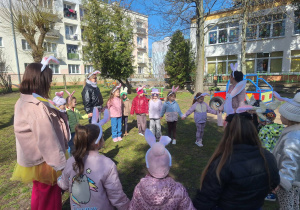 Grupa dzieci stojąca w kręgu z paniami przebranymi za zajączki.