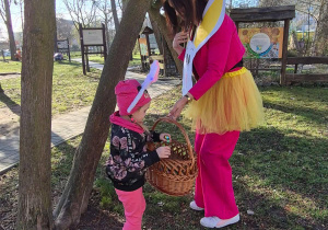 Dziewczynka wkładająca czekoladowe jajko do koszyka trzymającego przez zajączka wielkanbocnego.