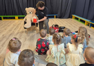 Dzieci patrzące na panią trzymającą misia, którego opatruje.