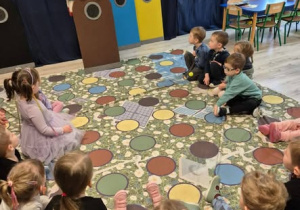 Pani trzymająca brązowy kosz na śmieci. Dzieci słuchające warsztatów.