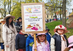 Grupa dzieci i i seniorów w kapeluszach podczas marszu w parku.
