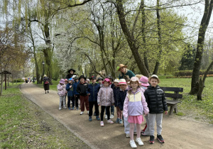 Grupa dzieci i i seniorów w kapeluszach podczas marszu w parku.