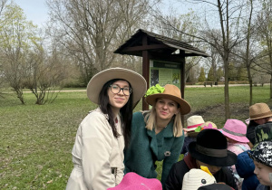 Dwie kobiety w kapeluszach wokół dzieci na tle parku.