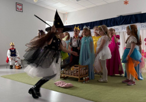 Dziewczynka przebrana za czarownice biegnąca. W tle dzieci przebrane w dworskie stroje.