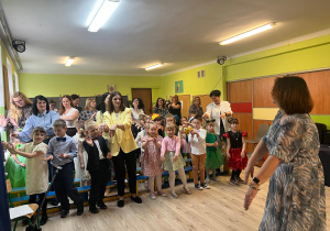 Grupa dzieci wraz z dorosłymi klaszcząca w dłonie, przed nimi prowadząca zabawę pokazująca ruchy.