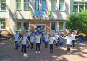 Dzieci tańczące podczas występu. Ubrane w białe koszulki trzymające kolorowe pompony.