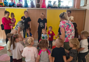 Dzieci z rodzicami stoją w kole i trzymają się za ręce.