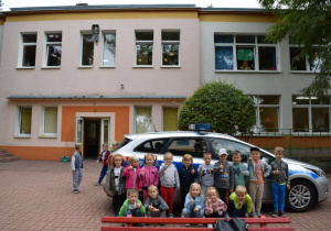 Przedszkolaki z grupy słoneczka stoją przed radiowozem policyjnym.