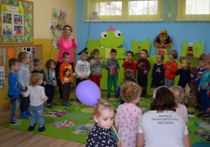 Rodzice i dzieci uczestniczą w zabawie zorganizowanej przez nauczycielkę.