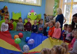 Dzieci z nauczycielką bawią się z chustą animacyjną i balonami.
