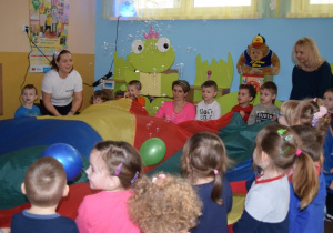 Dzieci z nauczycielką bawią się z chustą animacyjną i balonami.