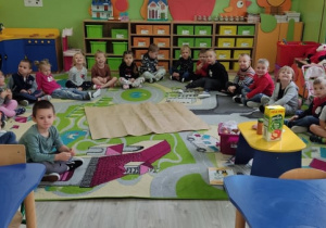 Dzieci siedzą na dywanie i czekają na zajęcia.