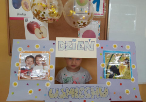 Dziecko pozuje do zdjęcia w ramce z napisem "Dzień uśmiechu".