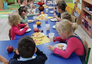 Dzieci przy stolikach zjadają słodki poczęstunek.