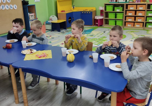 Dzieci przy stolikach zjadają słodki poczęstunek.