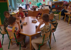 Dzieci zjadają słodki poczęstunek przy stolikach.