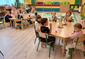 Dzieci zjadają słodki poczęstunek przy stolikach.