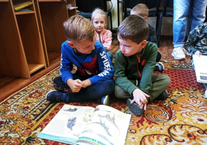 Chłopcy oglądają książkę o dinozaurach.