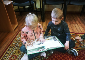 Dzieci oglądają książkę o dinozaurach.